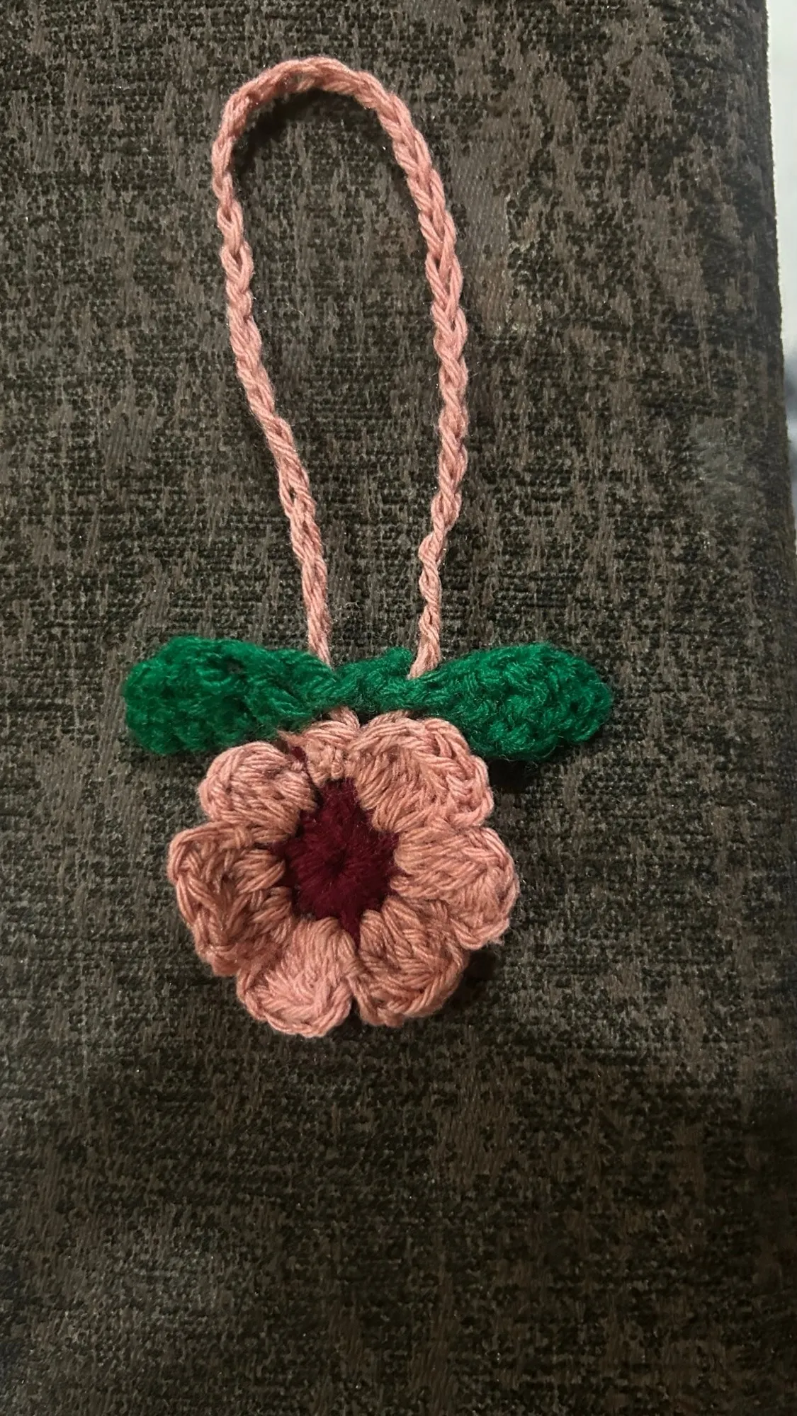 A dusty rose crochet flower bag charm with leaves