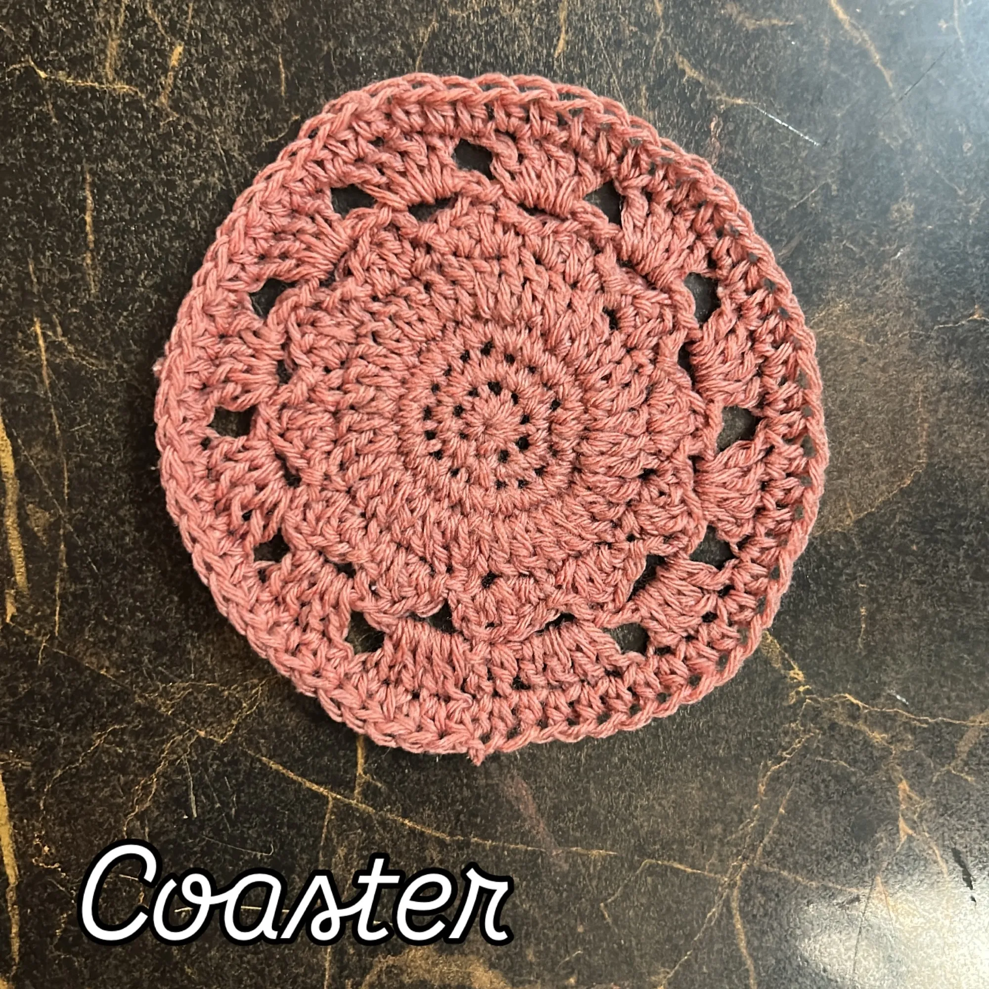 A round rose-pink crochet coaster with an open, scalloped edge