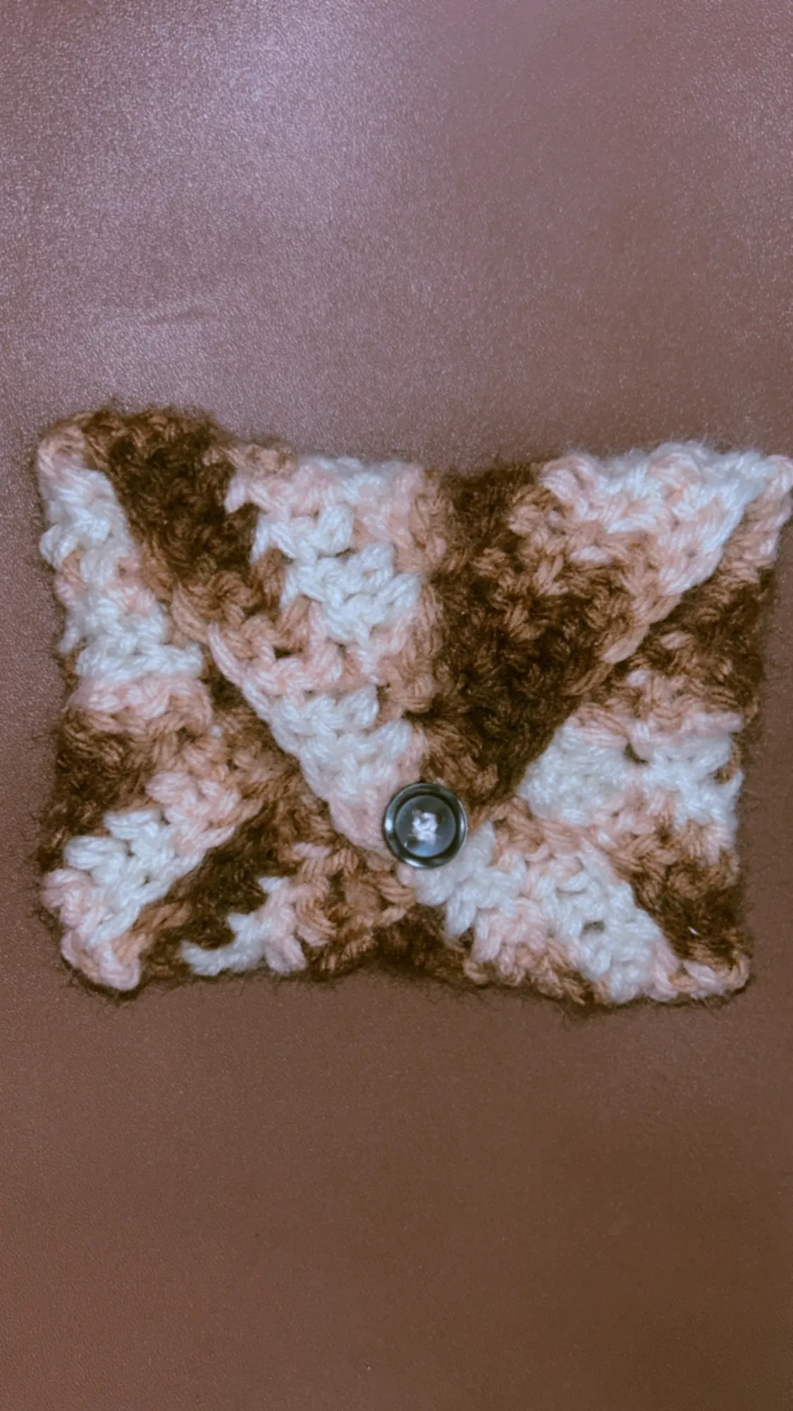 A dark brown crochet bookmark with a cream flower