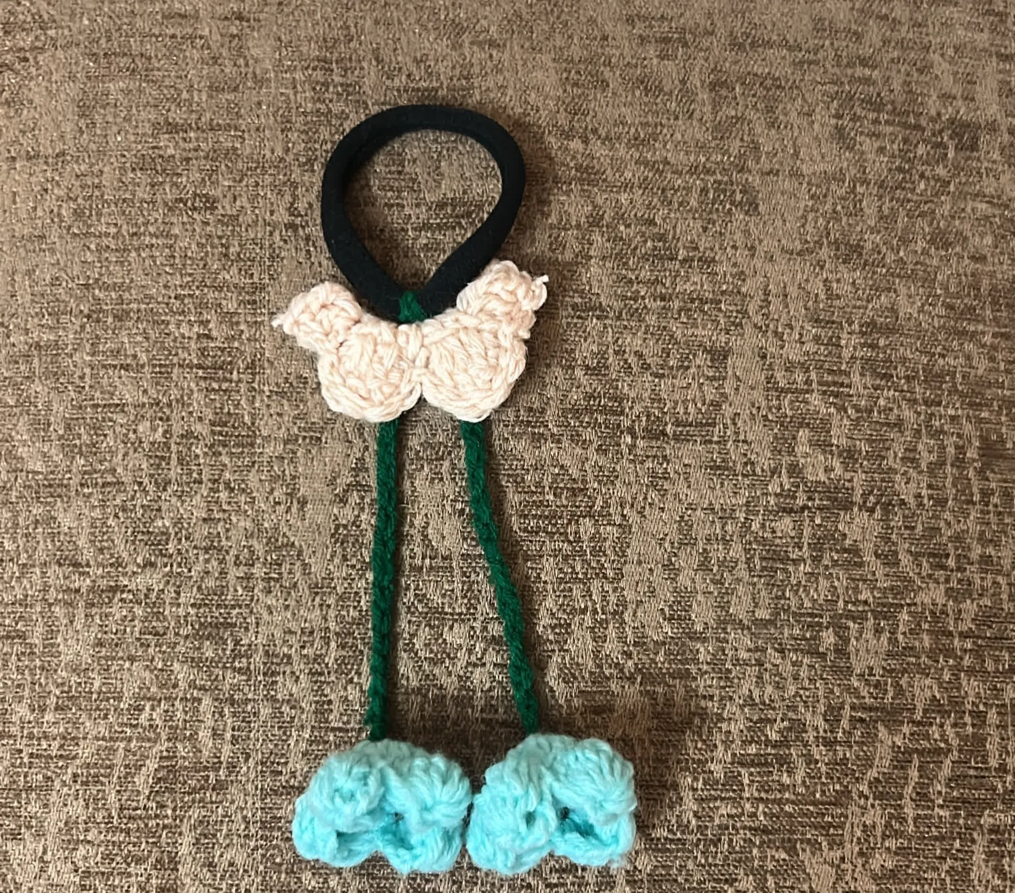 A black crochet hairtie topped with a cream butterfly and aqua blossoms