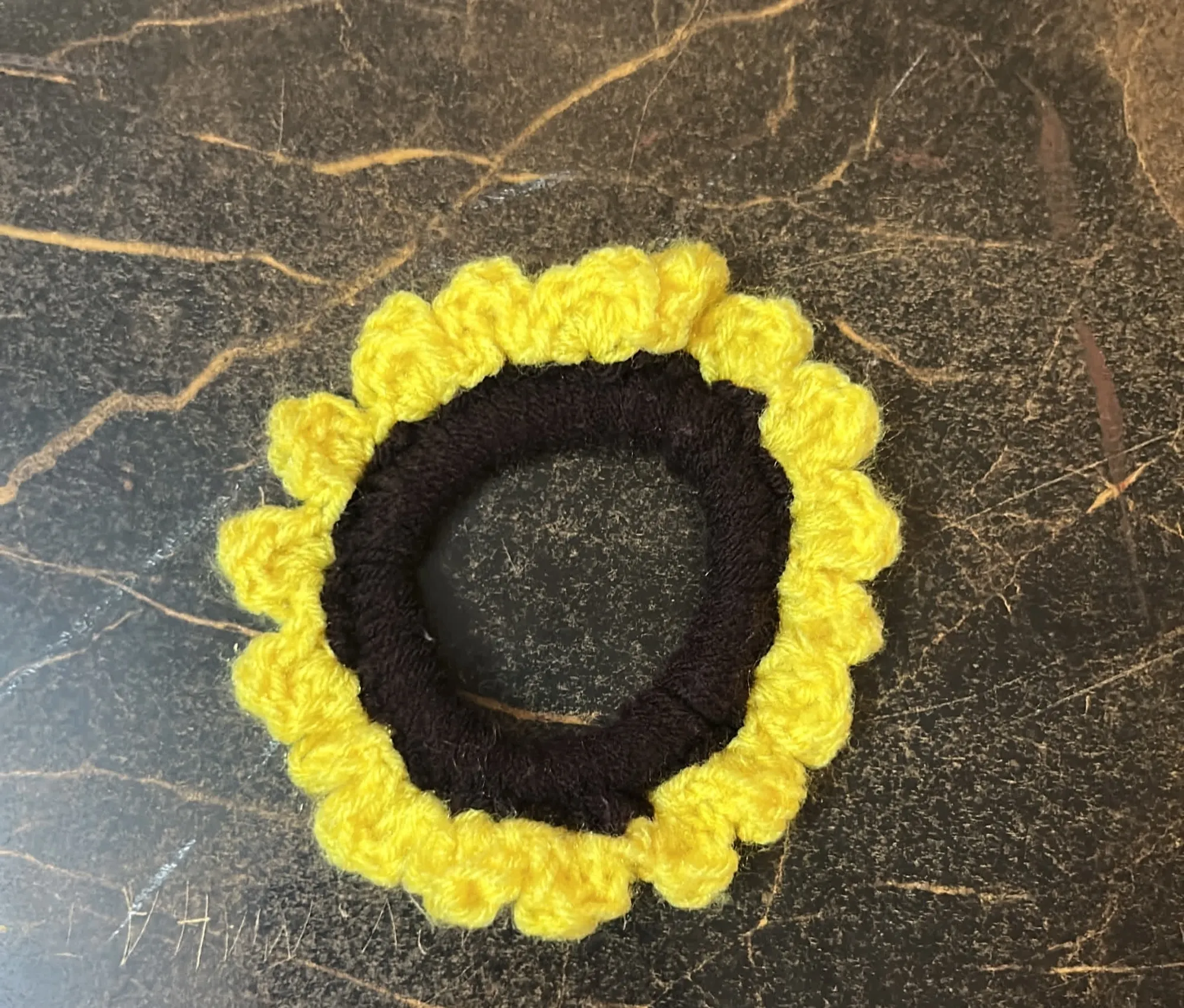 A yellow sunflower crochet scrunchie with a dark centre