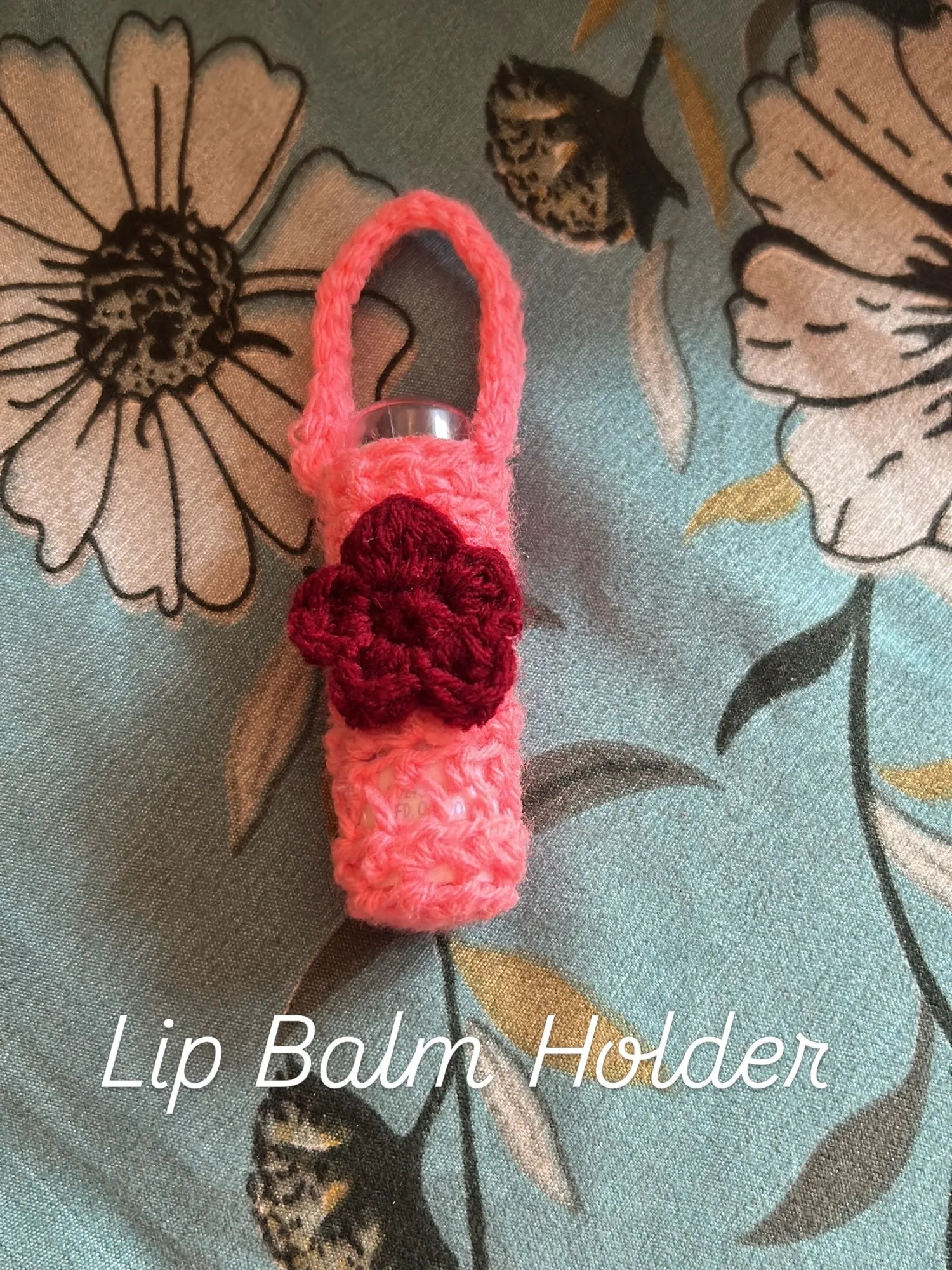 A pink crochet lip balm holder with a deep red flower and a hanging loop