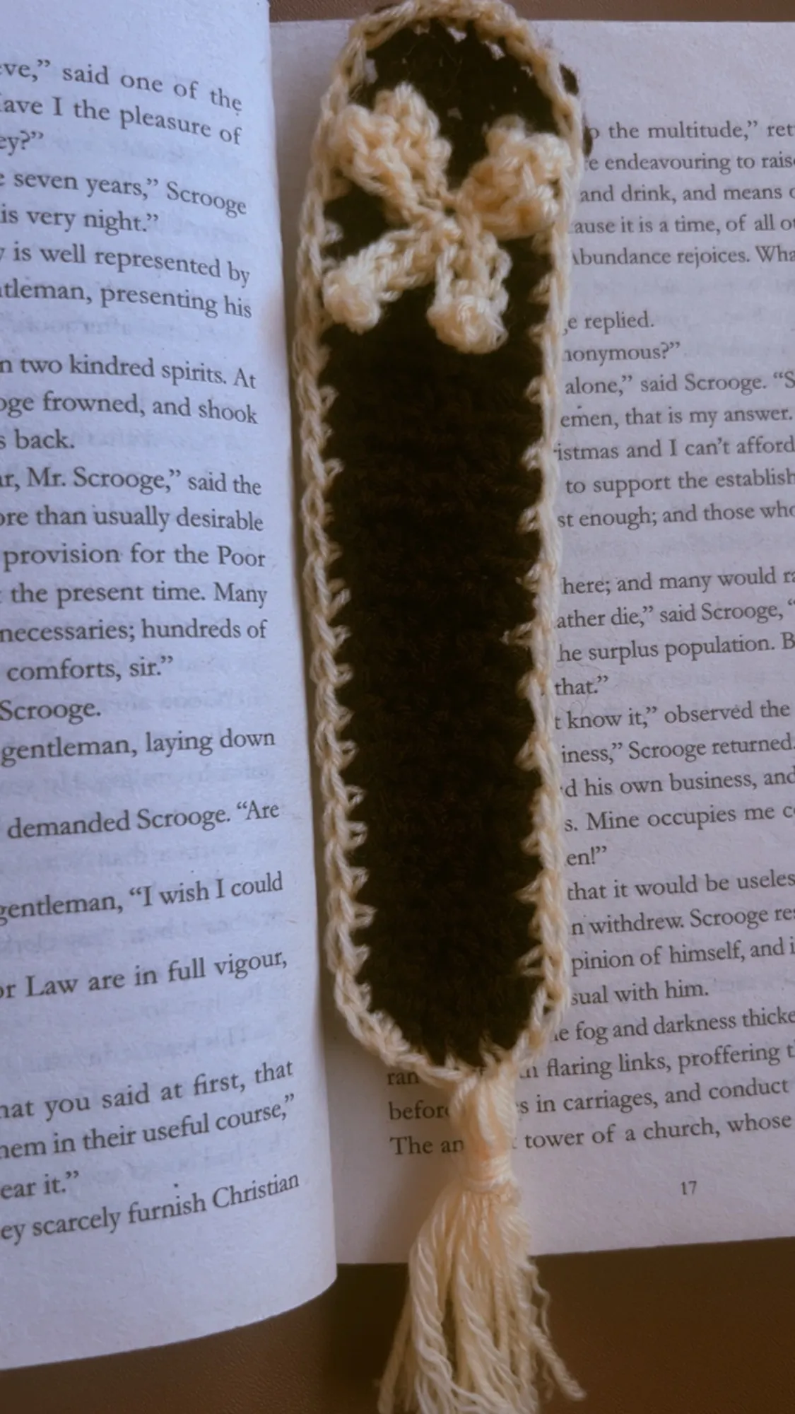 A dark crochet bookmark edged in cream, with a small flower and a tassel
