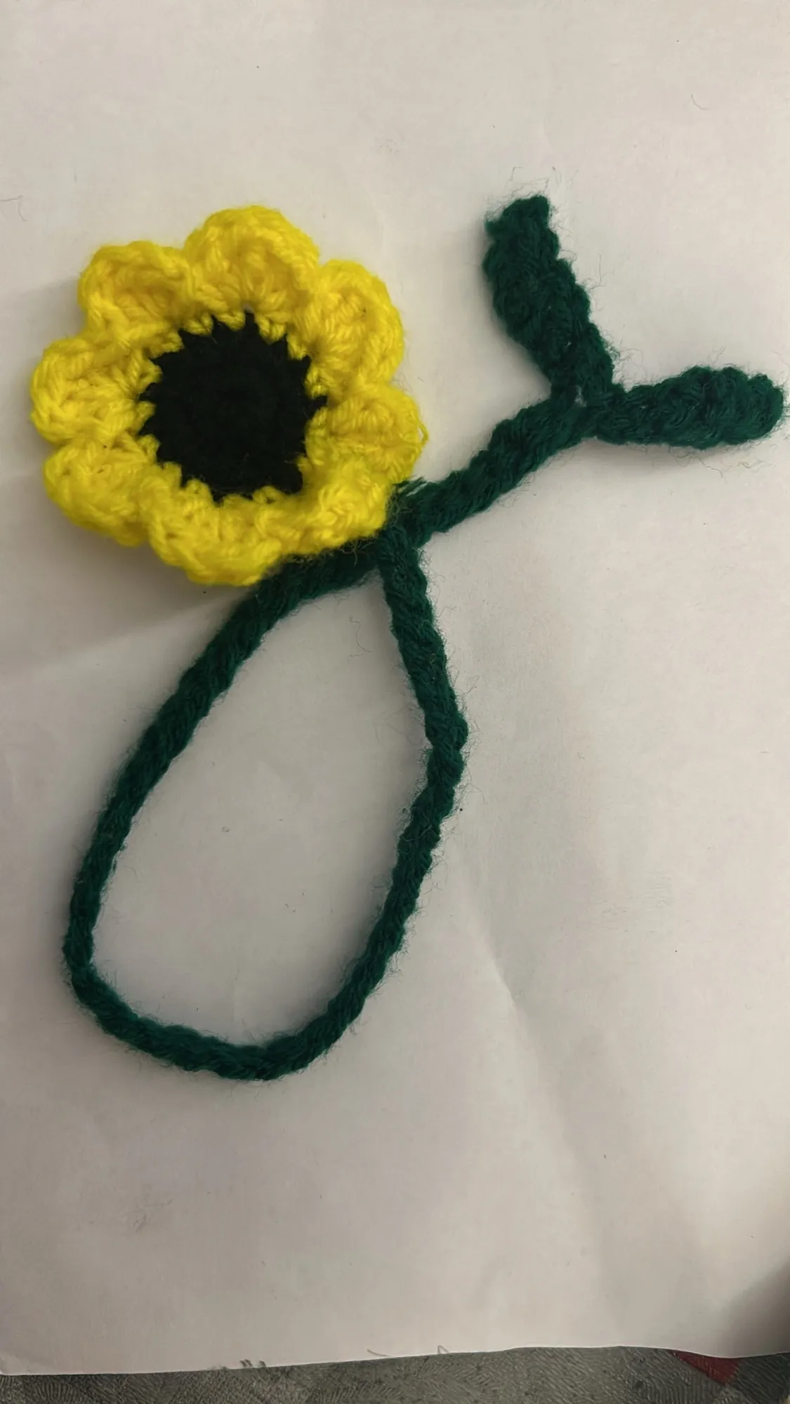 A crochet sunflower bookmark with a green stem