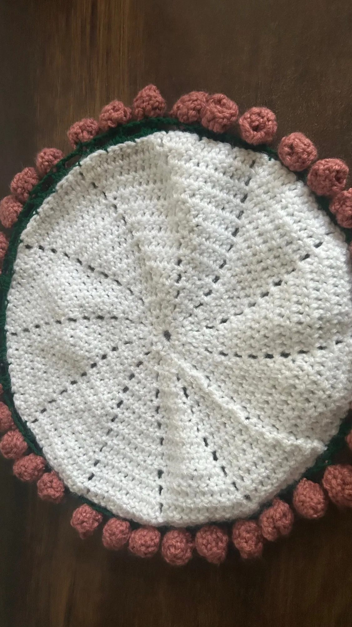 A round ivory crochet cushion cover trimmed with small rolled roses