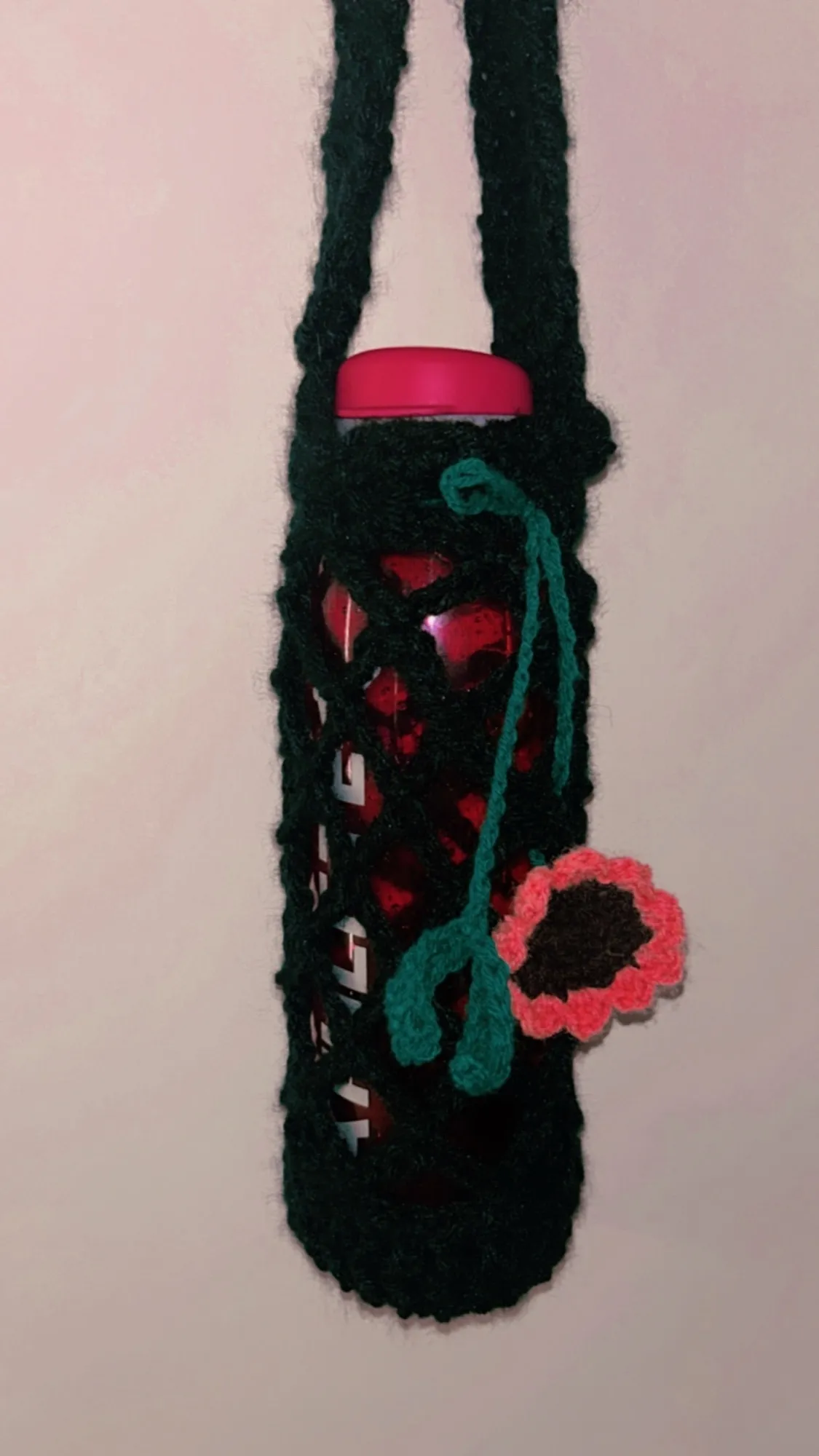 A black crochet water bottle sling with a coral flower