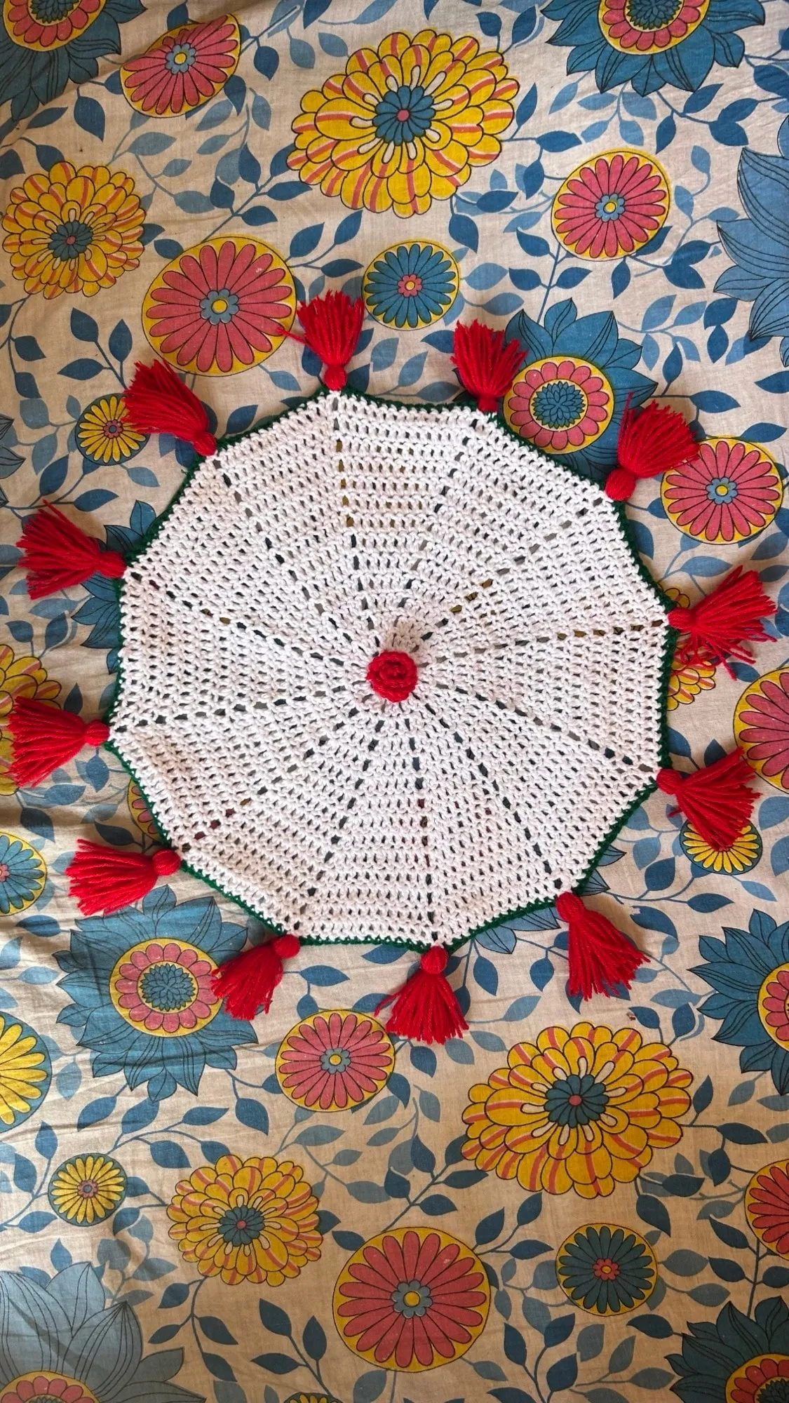 A circular crochet plate cover with a red tassel fringe